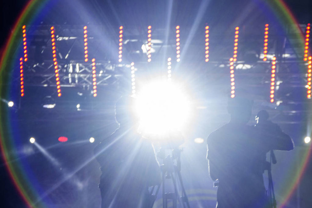 Imagen borrosa de la silueta de dos videógrafos en un escenario de concierto contra una hermosa luz brillante
. - Foto, imagen