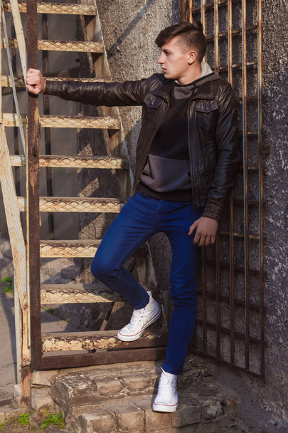stylish young brunet in leather jacket standing near wall - Fotó, kép