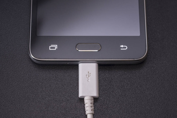 Beyaz kablo siyah zemin üzerine siyah smartphone - Fotoğraf, Görsel