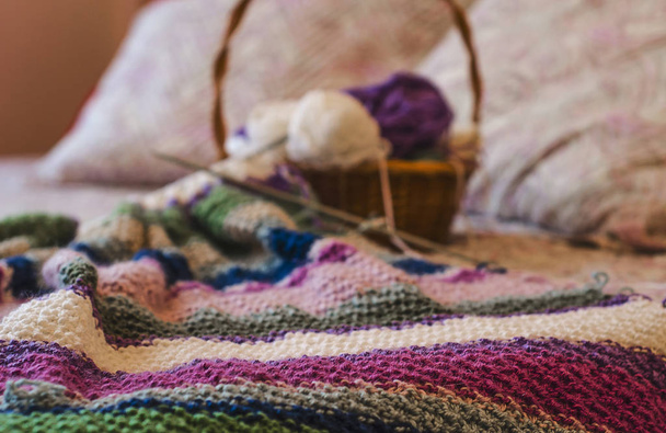 Tricot à rayures colorées à carreaux et panier avec fil et aiguille sur le lit
 - Photo, image