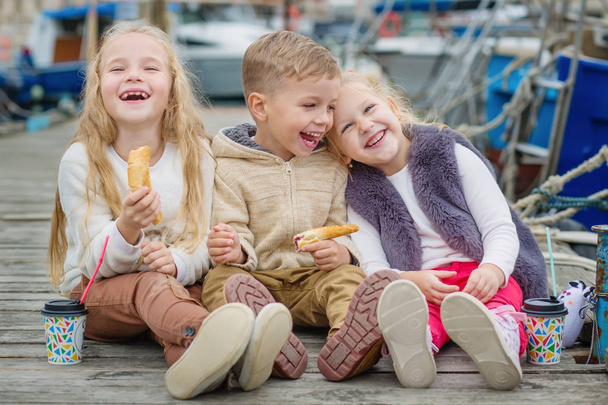 Tres niños felices sentados en el muelle y merienda
 - Foto, Imagen