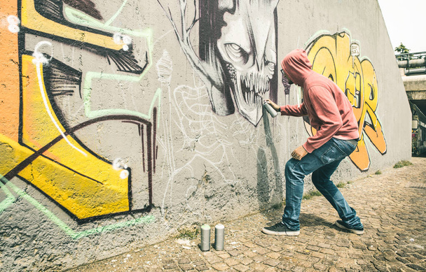 Street artist painting colorful graffiti on generic wall - Modern art concept with urban guy performing and preparing live murales with multi color aerosol spray - Contrast retro vintage filter - Photo, Image