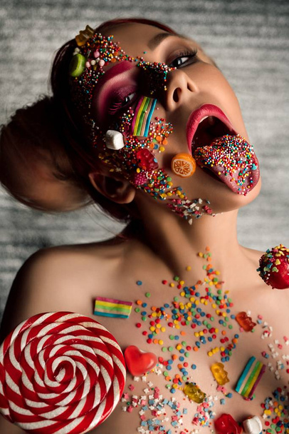 Chica delgada con caramelo en la cara, el cuerpo y la lengua - Foto, imagen