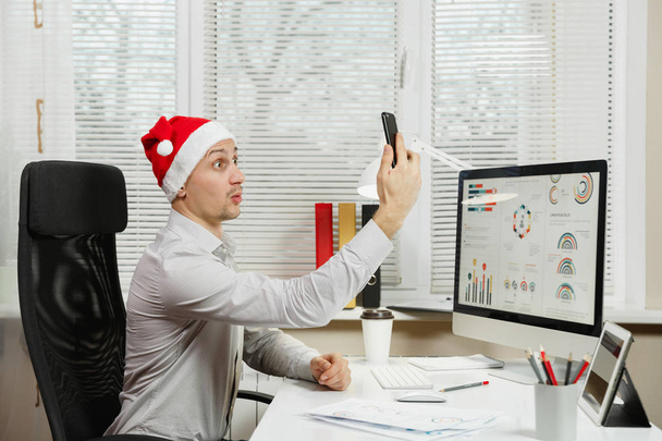 Beau homme d'affaires souriant en chemise et chapeau de Noël rouge assis
 - Photo, image