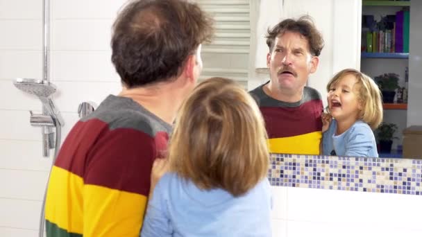 Niña riendo abofeteando padre en la cara jugando delante del espejo feliz - Metraje, vídeo