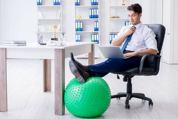 Young businessman doing sports stretching at workplace - Foto, Bild