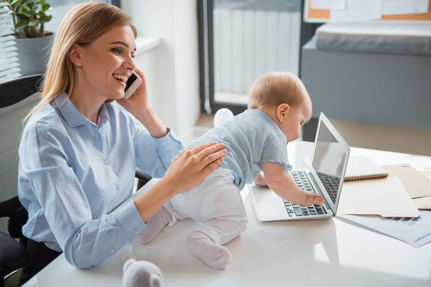 Glad mother working with baby in office - Фото, изображение