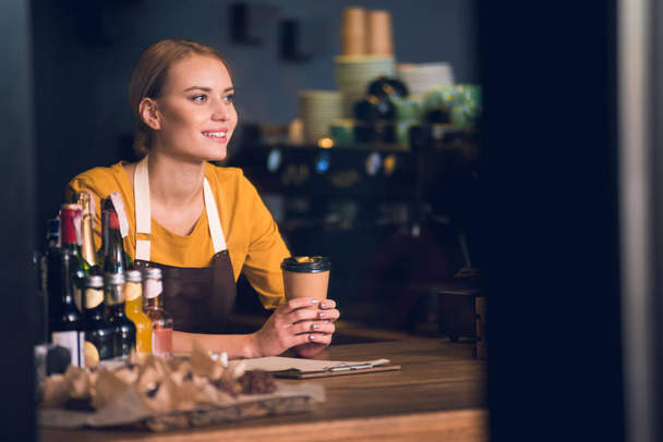 Cheerful female barista drinking cup of coffee - Foto, Bild