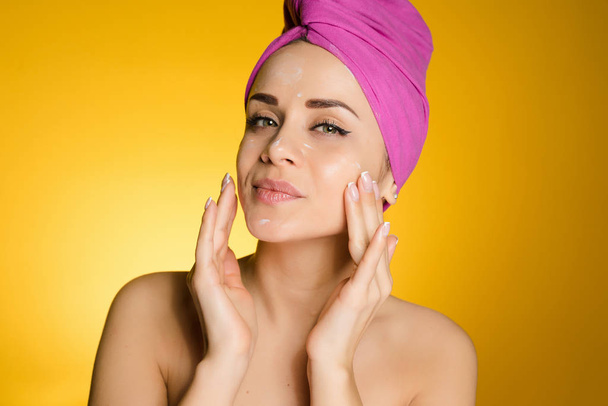 attractive girl with a pink towel on her head, puts a moisturizer on her face - Fotoğraf, Görsel
