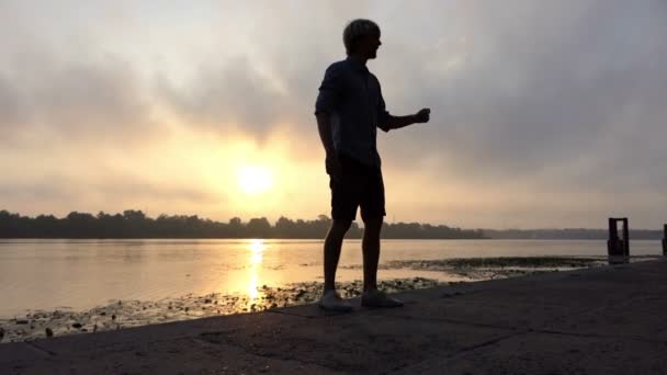 Atleet draait gelukkig op een rivieroever met Reed bij zonsondergang in Slow Motion - Video