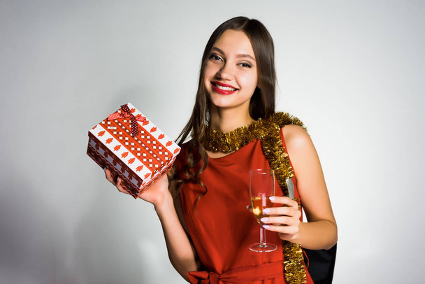 lächelndes attraktives Mädchen mit goldenem Lametta am Hals, das das neue Jahr 2018 feiert, mit einem Glas Champagner und einem Geschenk - Foto, Bild