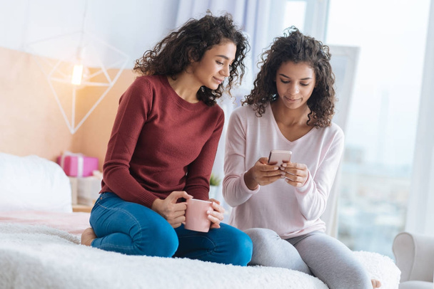 Relaxed young ladies looking at smartphone while sitting on bed - Photo, Image