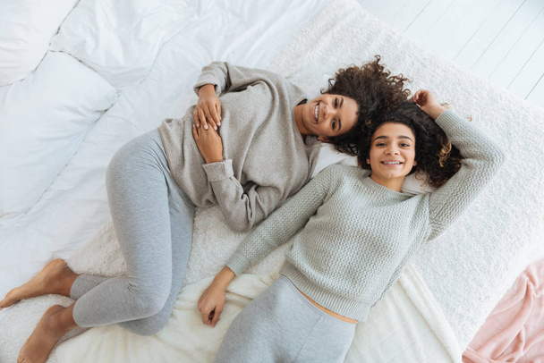 Cute sisters relaxing on bed and smiling cheerfully - Zdjęcie, obraz
