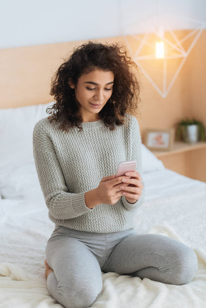 Beautiful girl using smartphone while sitting on bed - Foto, imagen
