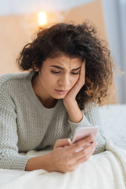 Confused curly haired girl looking at screen of smartphone - Photo, Image