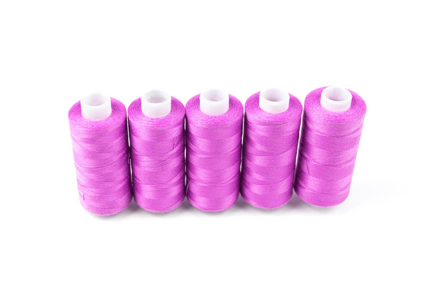 Five pink or magenta sewing threads in a row on a white coils on a white background. Sewing supplies and accessory, textile wallpaper - Photo, Image