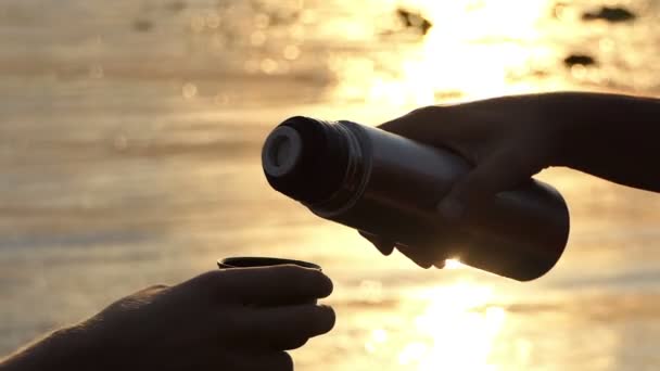 Мужские руки наливают воду из фляжки в чашку на берегу реки на Сансет в Сло-Мо
 - Кадры, видео