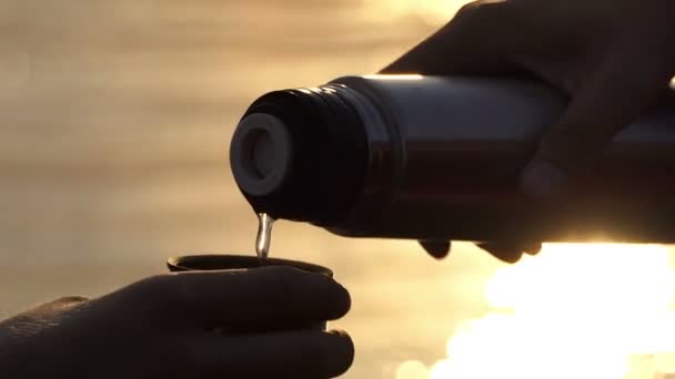 Manos de hombre vierten agua de un frasco en una taza en una orilla del río al atardecer en Slo-Mo
 - Metraje, vídeo