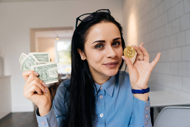 successful smart young girl in a blue shirt is holding a golden bitcoin and dollars - Foto, Imagem