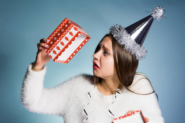 sad young girl in a festive hat holds an empty gift box, she does not have a gift - Fotoğraf, Görsel