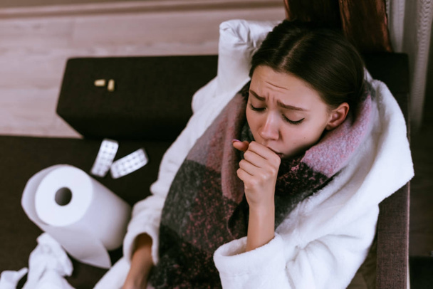 sad young girl is very sick, sore throat, neck warm scarf, coughs, drinks tablets - Fotó, kép