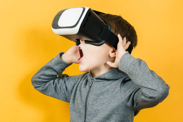 Boy with a headset of virtual reality. Innovative technology. On an orange background. - Photo, Image