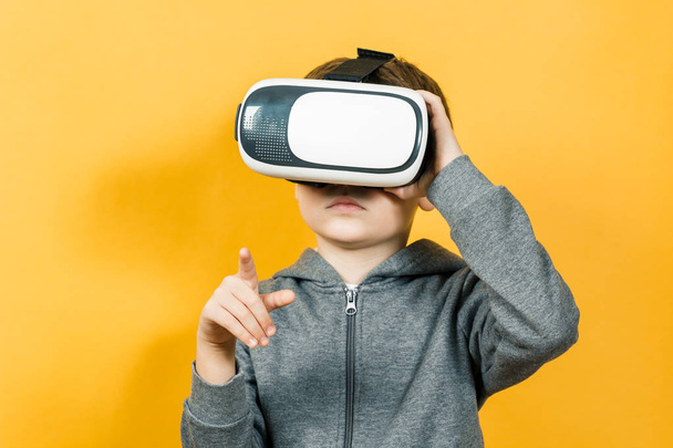 Jongen met een headset van virtual reality. Innovatieve technologie. Op een oranje achtergrond. - Foto, afbeelding