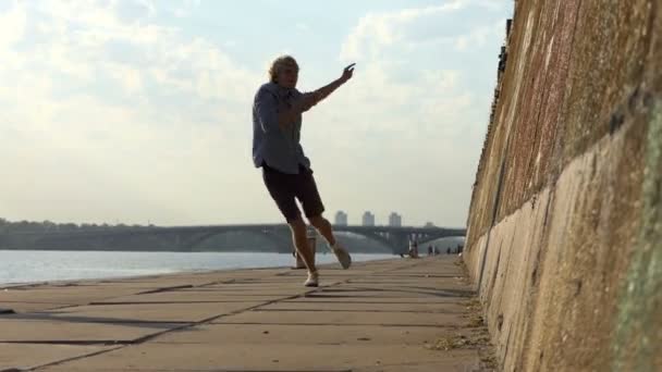 Happy Man baila Disco en una orilla del río con una pared de piedra alta en verano
 - Imágenes, Vídeo