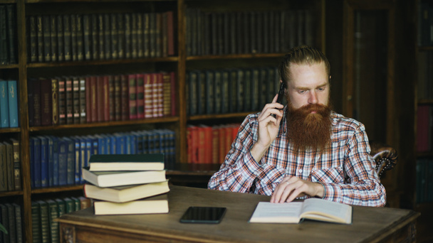Joven estudiante barbudo hablando por teléfono mientras se prepara para los exámenes en la biblioteca de Univercity
 - Foto, Imagen