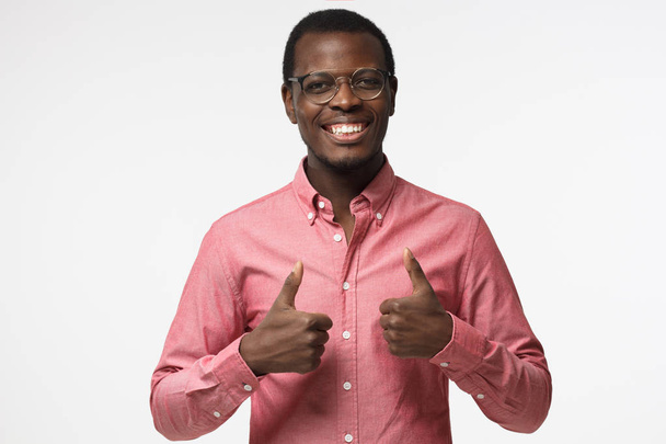 Closeup of young optimistic afrcian american business man isolated on grey background showing thumps up with positive emotions of content and happiness. Concept of recommendation - Foto, afbeelding