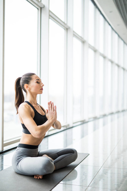 Schönheit junge Frau praktiziert Yoga in der Lotusposition vor Panoramafenstern - Foto, Bild