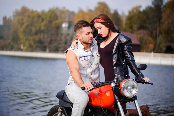 pareja elegante y de moda en el amor en una motocicleta coqueteando primer plano en un fondo de finales de otoño en el parque
 - Foto, Imagen