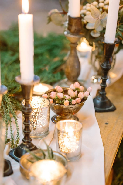 christmas, celebrating, decoration concept. on wooden feast table prepared for dinner there are lots of candles and fresh emerald conifers branches on white silk drapping - Foto, immagini