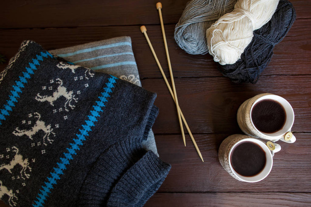 Χειμερινά Αξεσουάρ: πλεκτά ενδύματα, δύο φλιτζάνια καφέ, μπάλες από νήματα και βελόνες για πλέξιμο σε ξύλινο πλαίσιο. Χειμερινής περιόδου - Φωτογραφία, εικόνα