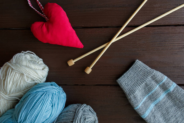 Аксессуары для вязания: шары из разноцветной пряжи, вязаный свитер и вязальные спицы на деревянном фоне
 - Фото, изображение