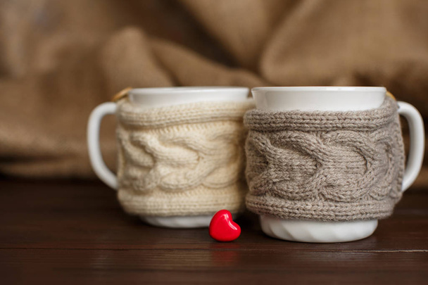 Φλιτζάνια καφέ με πλεκτό ποτηροθήκη κοντά στην καρδιά - συμβολίζοντας την αγάπη του καφέ - Φωτογραφία, εικόνα