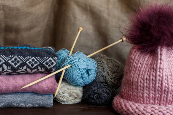 Knitting homemade, colorful knitted sweaters near pink hat and balls of yarn. Handmade knitwear - Photo, Image