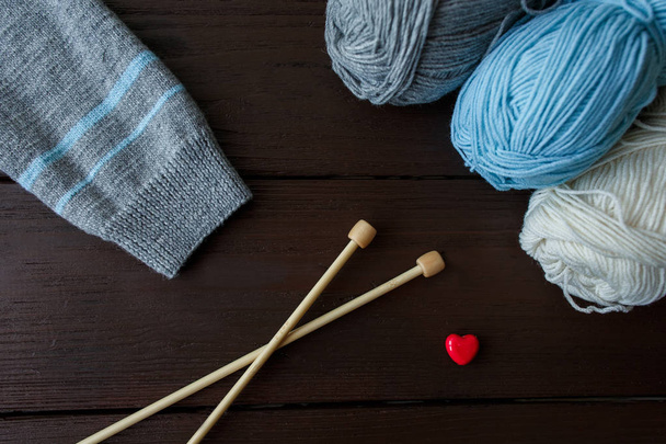 Knitting accessories: sleeve of knitted sweater, balls of yarn, needles for knitting and red heart symbolizing love to knitwear - Photo, Image