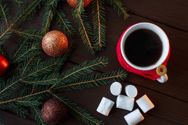 Kerstmis achtergrond, kopje koffie met rood gebreid bekerhouder in de buurt van marshmallow, kerstballen en kerstboom. Wintervakantie - Foto, afbeelding