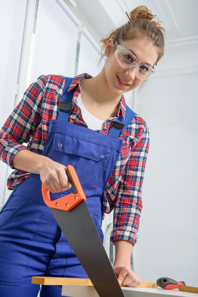 young woman carpenter cutting a board with handsaw - Foto, Bild