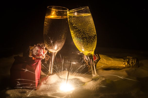 Φόντο εορτασμός Πρωτοχρονιάς με ζευγάρι φλάουτα και μπουκάλι σαμπάνιας με χαρακτηριστικά Χριστούγεννα (ή στοιχεία) σε χιονισμένο σκούρο τονισμένο ομιχλώδες φόντο. Επιλεκτική εστίαση. - Φωτογραφία, εικόνα