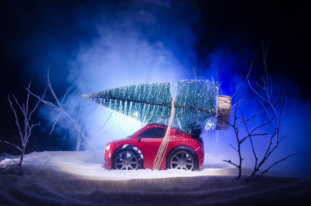 Coche miniatura con abeto en Snowy Winter Fores, o coche de juguete que lleva un árbol de navidad y por la noche
 - Foto, Imagen