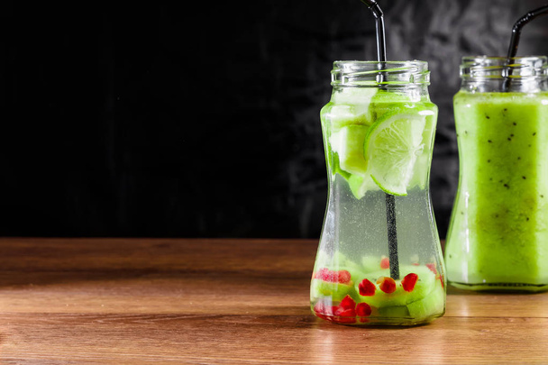 Refreshing drink from kiwi, green apple, lime, mint and pomegranate on a wooden table. The concept of a healthy diet, detox. - Фото, изображение