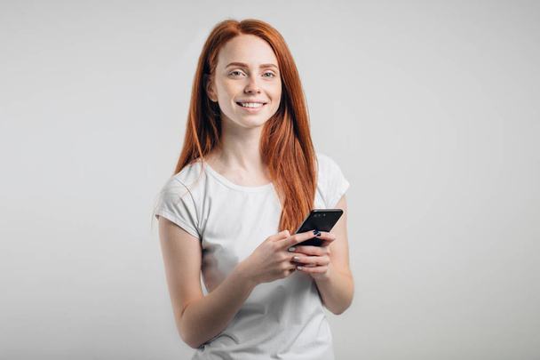 redhead girl with clean freckles skin using smartphone and looking at camera. - Photo, image
