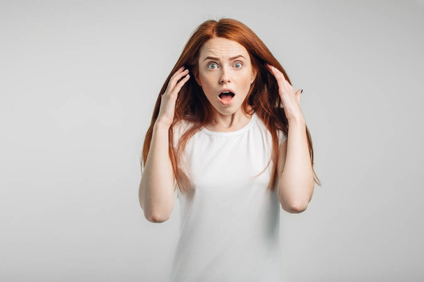 redhead girl on white background with strong expression of fear, round eyes - Foto, Imagem