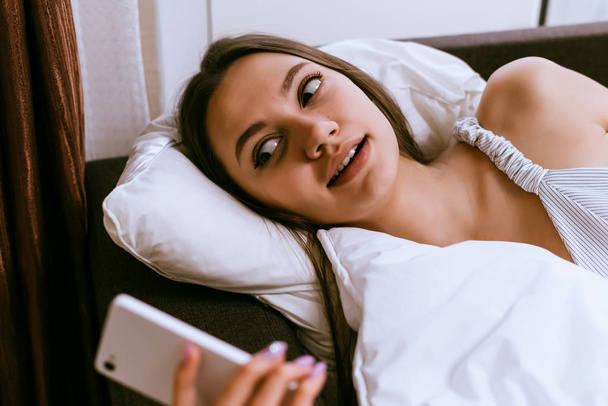 jong meisje ligt op bed, schakelt het alarm op de telefoon - Foto, afbeelding