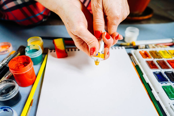 woman artist draws on white paper with oil paints, beside lie watercolor colors and gouache - Fotografie, Obrázek