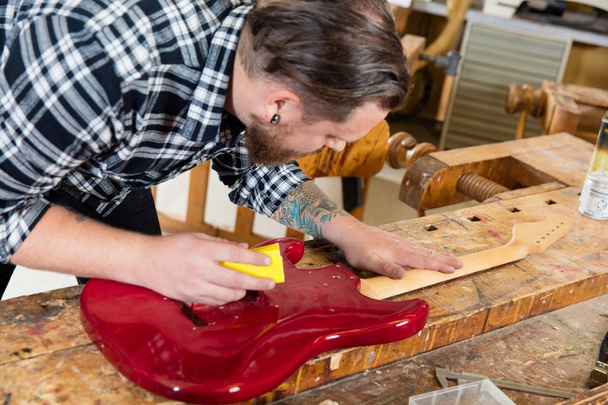 Primer plano del artesano lijando un cuello de guitarra en madera en el taller
 - Foto, Imagen
