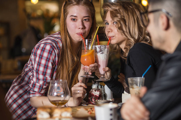 Young woman drinking milkshake while sitting with friends at cafe - Zdjęcie, obraz