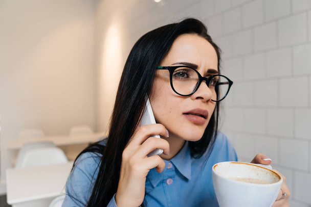 donna d'affari di successo riflessivo con gli occhiali sta tenendo colloqui importanti al telefono e bere caffè profumato
 - Foto, immagini